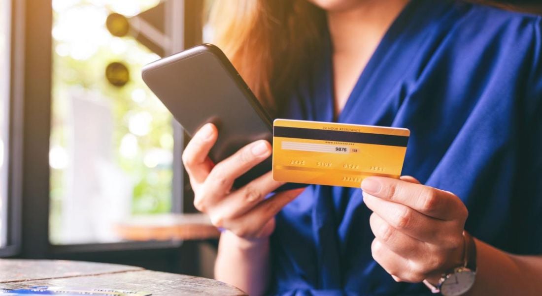 A woman holding a phone in one hand and a credit card in the other, showing her transferring money.