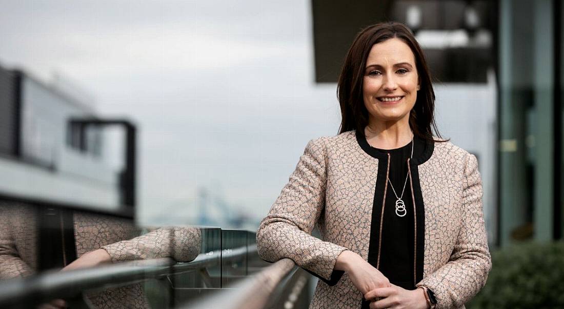 Aisling Campbell of Accenture standing leaning on a balcony railing outside with blurred buildings on the skyline behind her.