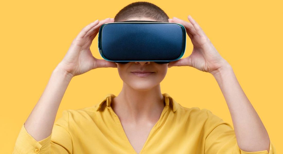 A woman wearing a yellow shirt wearing a VR headset against a yellow background, symbolising the metaverse.