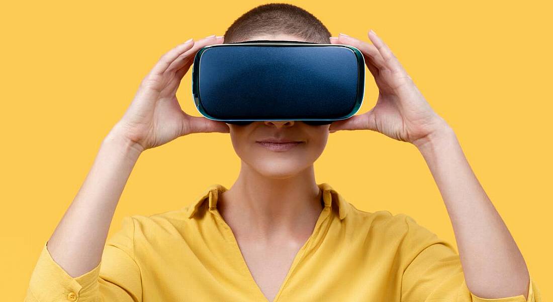 A woman wearing a yellow shirt wearing a VR headset against a yellow background, symbolising the metaverse.