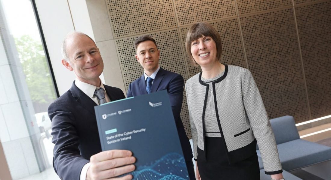 Two man and a woman standing in a group, one of the men on the left is holding a report about cybersecurity in Ireland.