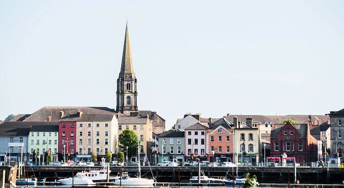 The skyline of Waterford across the River Suir, with boats moored in the foreground and the steeple of Christ Church Cathedral visible in the background.