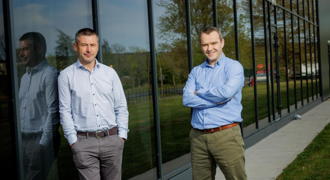 Two men in pale blue shirts stand outside a glass-fronted building.