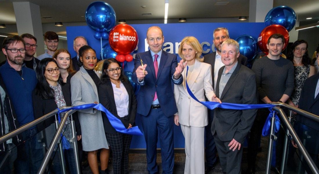 Micheál Martin cuts the ribbon on the new Blancco office opening as employees stand behind, celebrating with balloons.