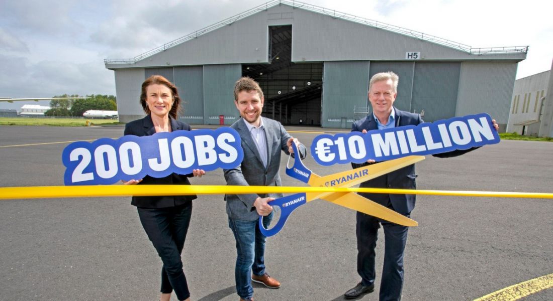 Shannon Group CEO Mary Considine, Ryanair director of operations Neal McMahon and Shannon Group COO Ray O’Driscoll. Ray is holding a €10 million sign, Mary is holding a 200 jobs sign while Neil is cutting a yellow ribbon. An airline hanger is in the background.