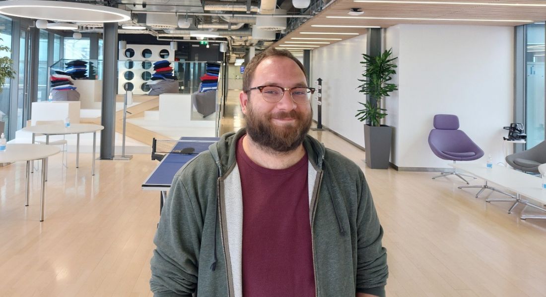 A man wearing a grey hoody and wine T-shirt smiles at the camera while standing in the Yahoo office in Dublin.