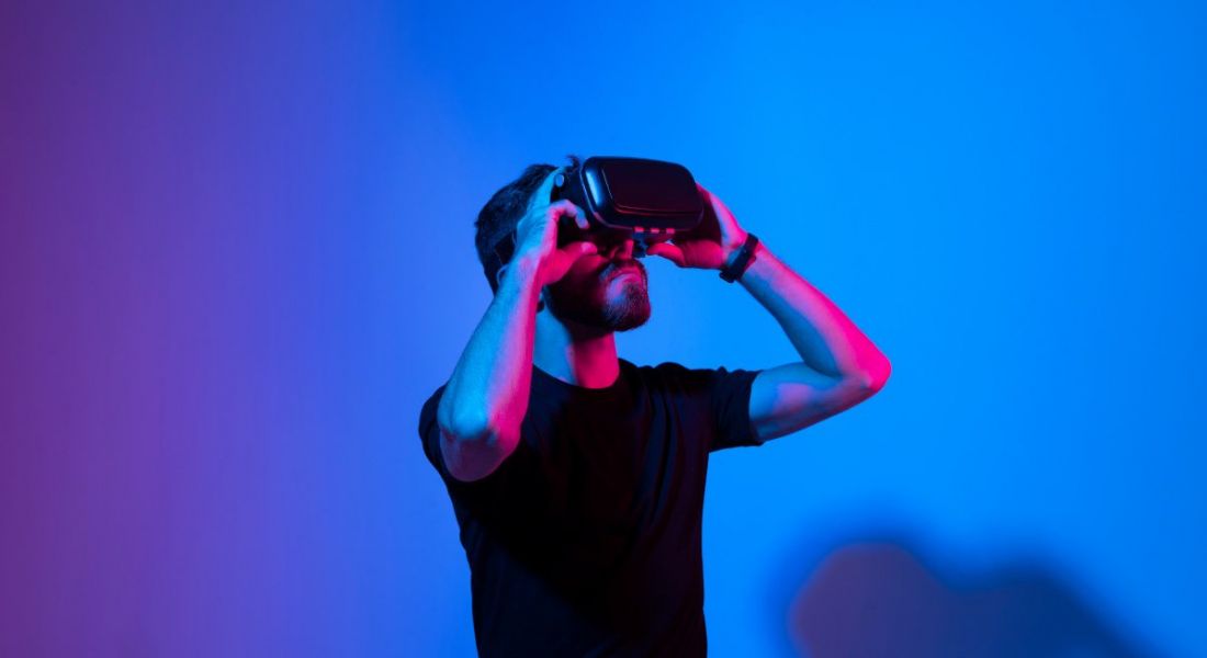 A young man in a black t-shirt wearing a virtual reality headset against a blue background.