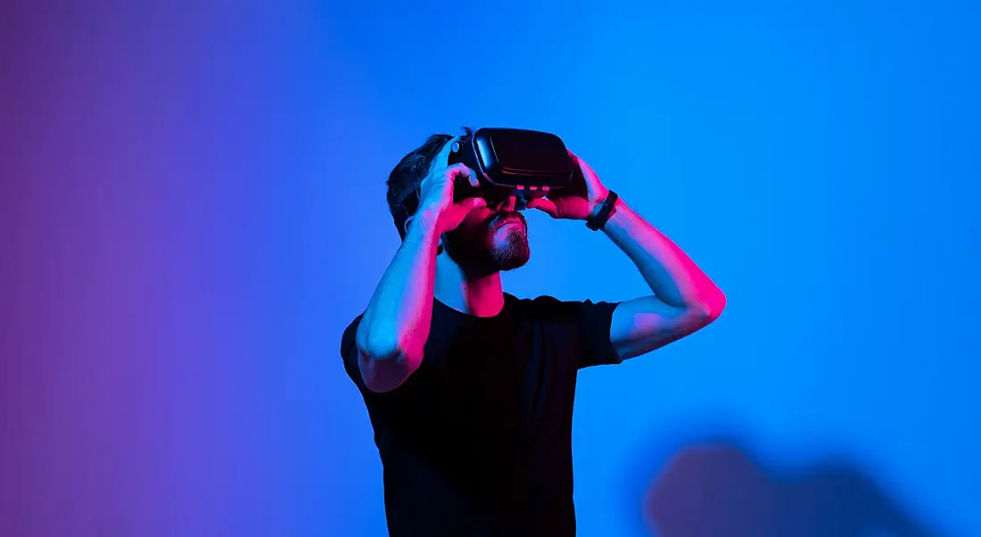 A young man in a black t-shirt wearing a virtual reality headset against a blue background.