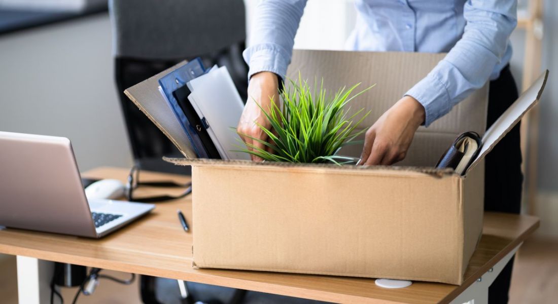 A woman putting a plant into a box of files on a desk, symbolising quitting your job.