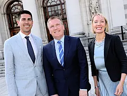 Neil Phelan dressed in a navy suit with spotted shirt and pocket square stands in front of a wall branded with the HCS logo.