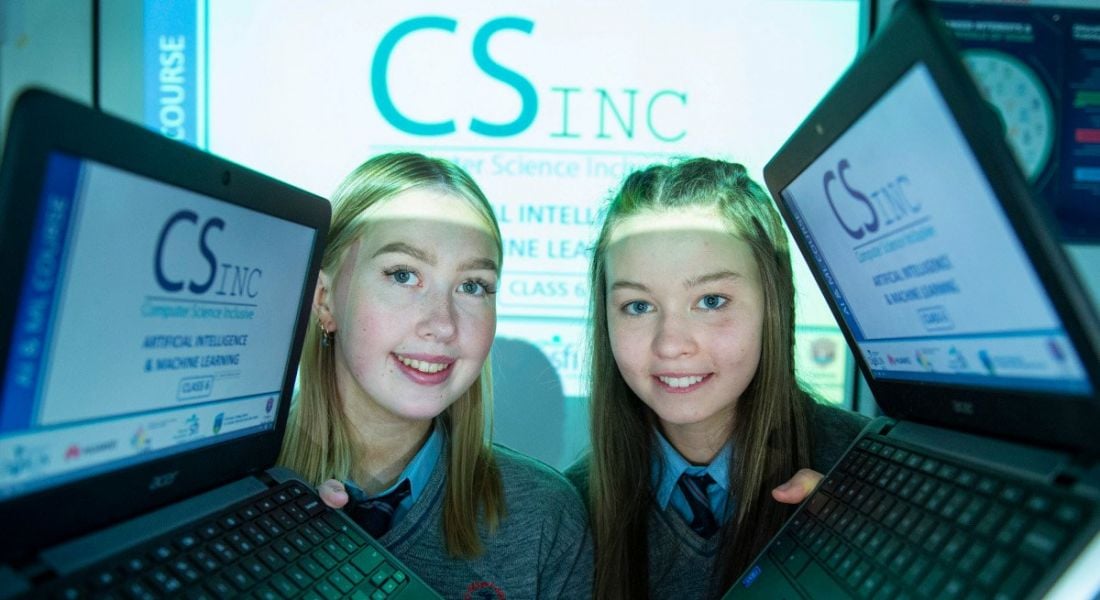 Two young women holding up laptops with the machine learning and AI course developed by SFI and TU Dublin's CSinc displayed on the screen.