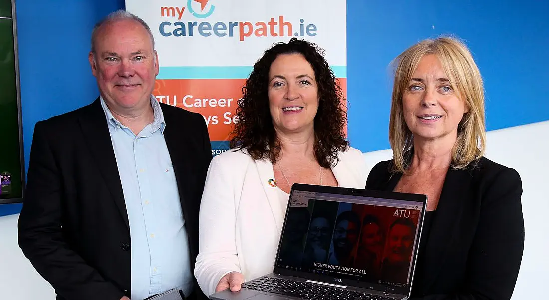 A man and two women standing in front of a poster for the ATU MyCareerPath.ie site. One woman is holding a laptop.