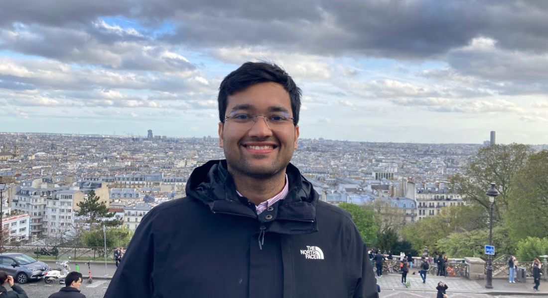 A young man wearing a navy hoody smiles at the camera against the backdrop of a city. He is a product engineer at Intercom.