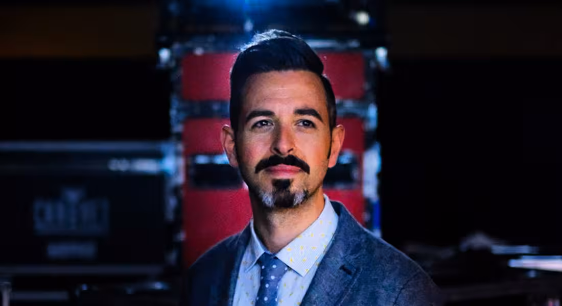 A headshot of Rand Fishkin standing in a darkened room.
