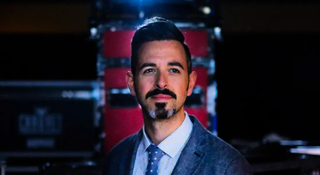 A headshot of Rand Fishkin standing in a darkened room.