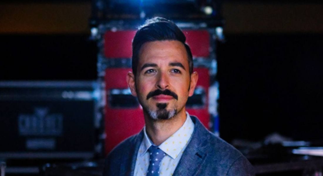 A headshot of Rand Fishkin standing in a darkened room.