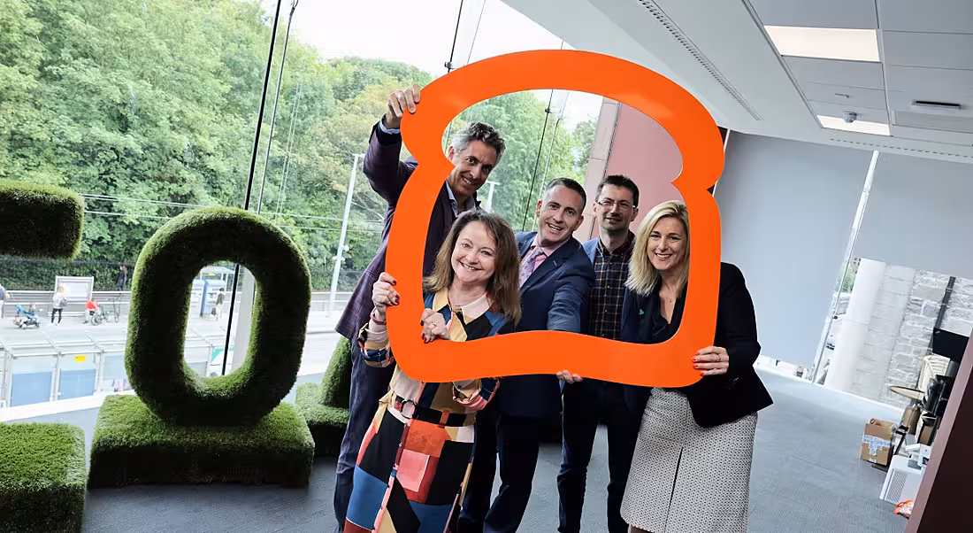 A group of people stand together framed by a large 3D outline of a toast slice. The windows behind them overlook Dublin’s St Stephen’s Green.