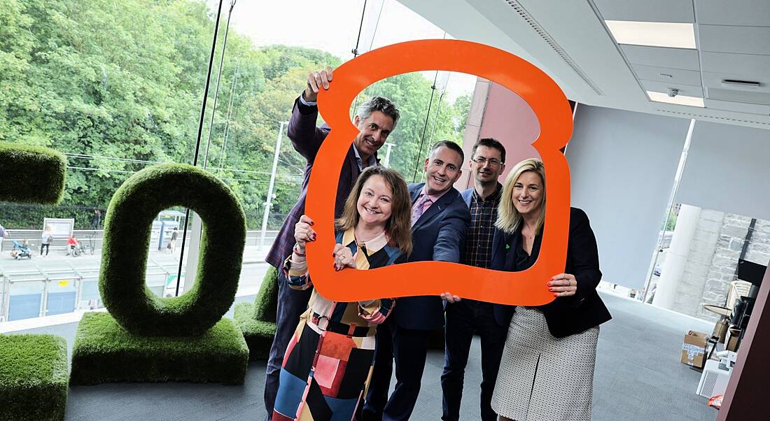 A group of people stand together framed by a large 3D outline of a toast slice. The windows behind them overlook Dublin’s St Stephen’s Green.