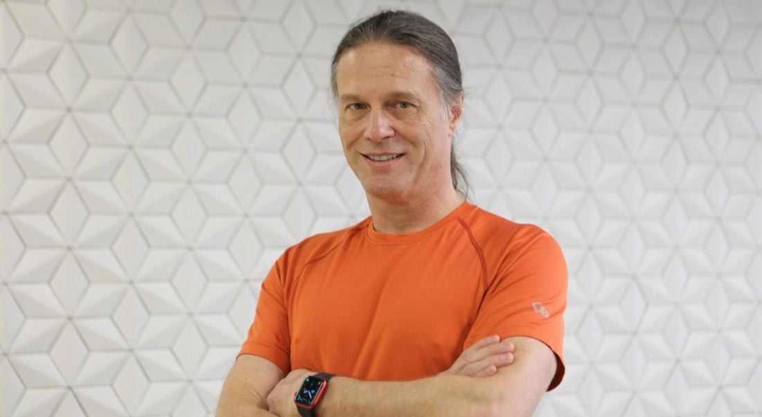 Yahoo's Nate McCoy stands against a white wall with a geometric pattern smiling at the camera. He is wearing an orange t-shirt.