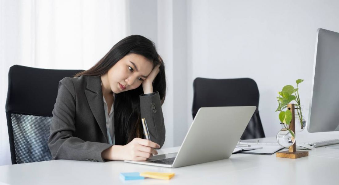 A stressed out young woman sitting in front of a laptop and taking notes.