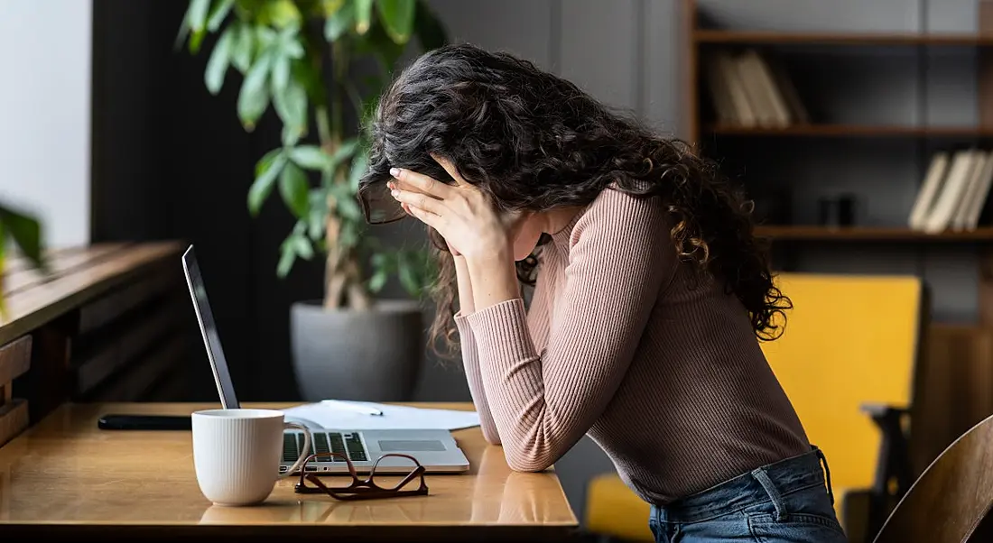 A young woman with her head in her hands while sitting at a desk, showing a lack of psychological safety at work.