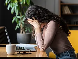 A stressed out young woman sitting in front of a laptop and taking notes.