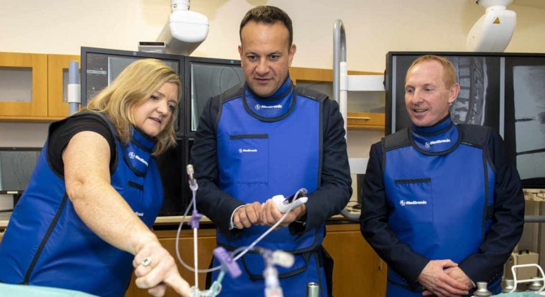 Tanaiste Leo Varadkar with two Medtronic Galway representatives in blue uniform jackets looking at medical devices.