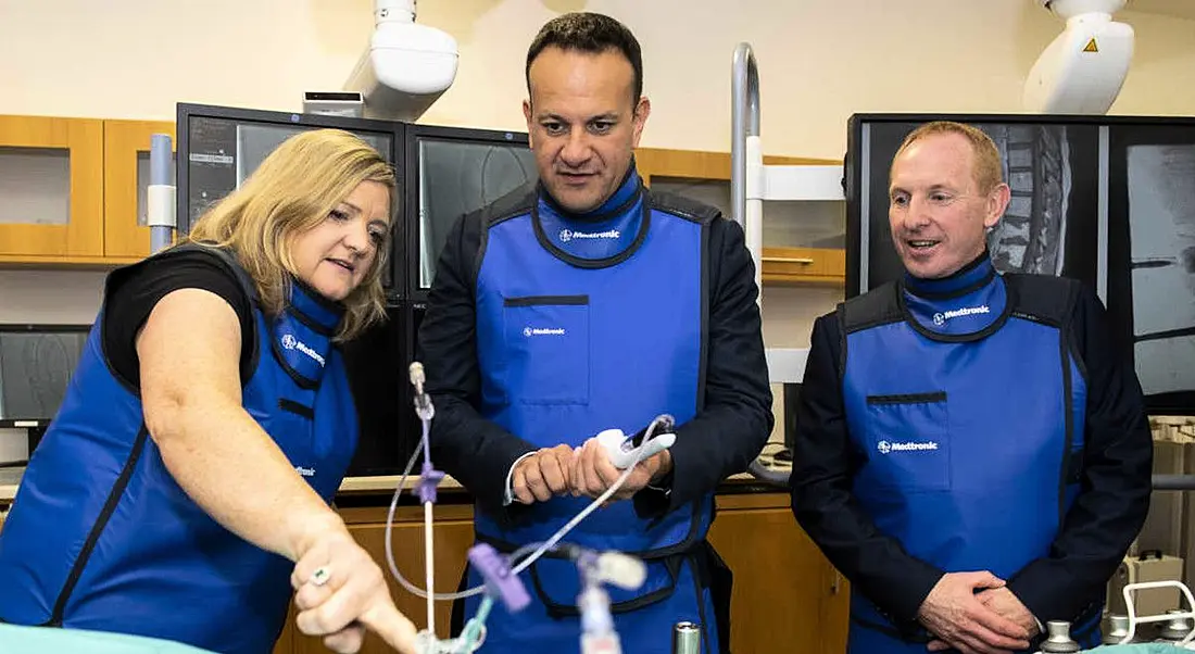 Tanaiste Leo Varadkar with two Medtronic Galway representatives in blue uniform jackets looking at medical devices.