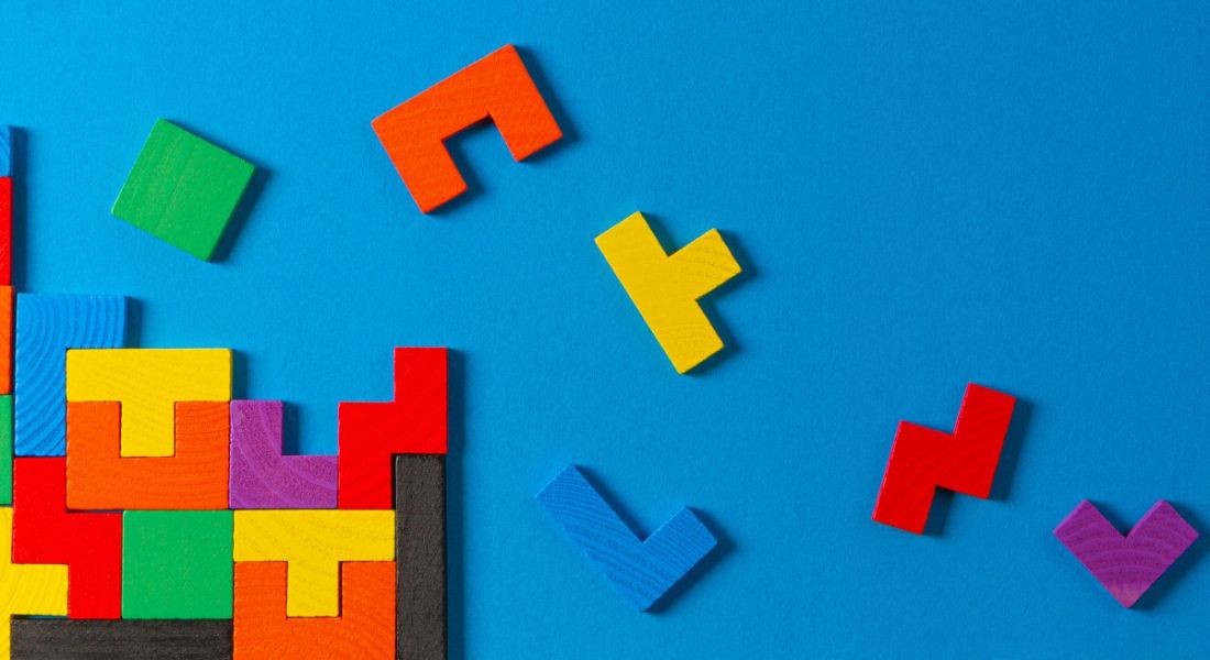 Several wooden blocks with different shapes and colours fit together. More are scattered against a blue background, representing a neurodiverse workforce.