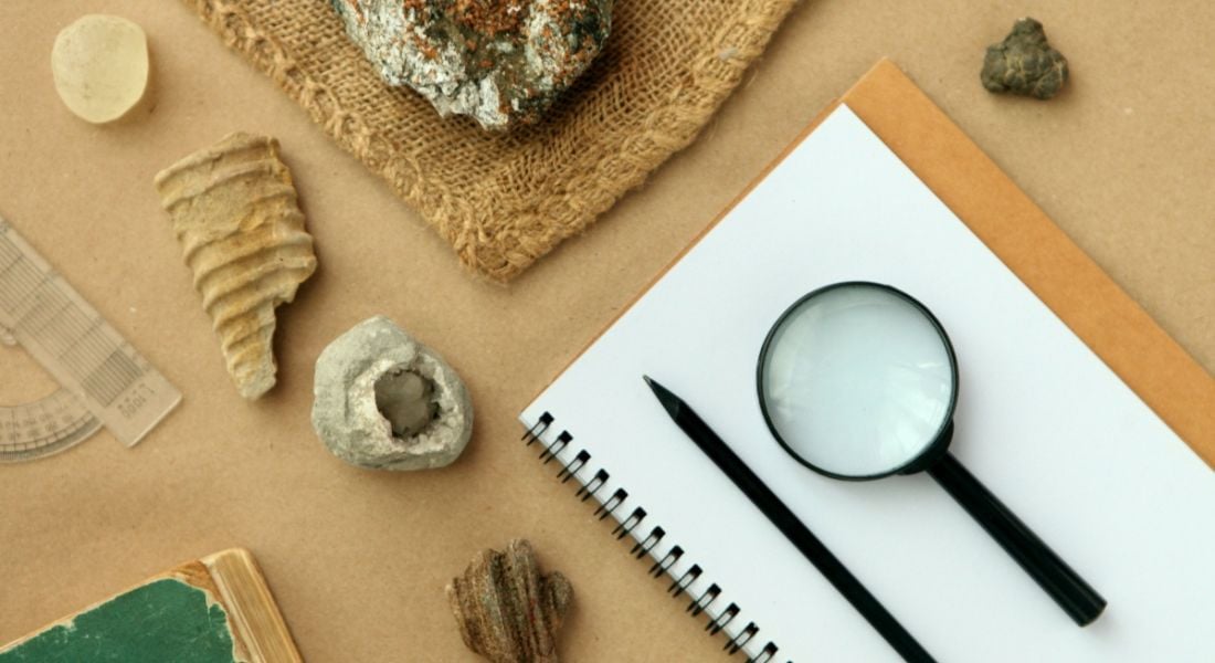 Geology samples laid out on a table with a notebook and pen and magnifying glass.