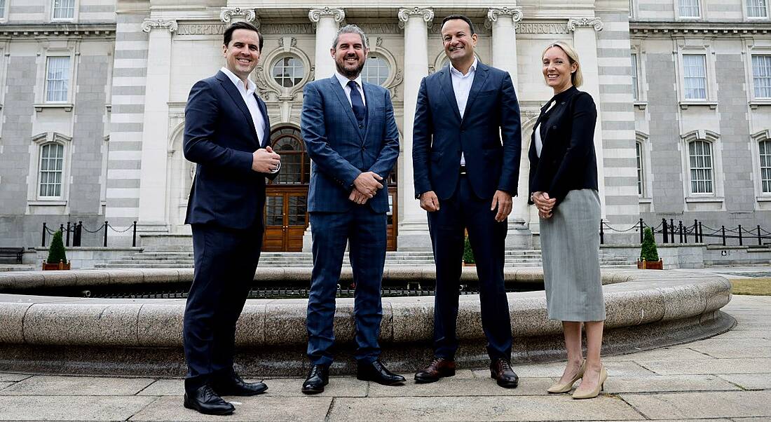 Three men and one woman standing outside a stone building to celebrate the announcement of 250 jobs at Kaseya.