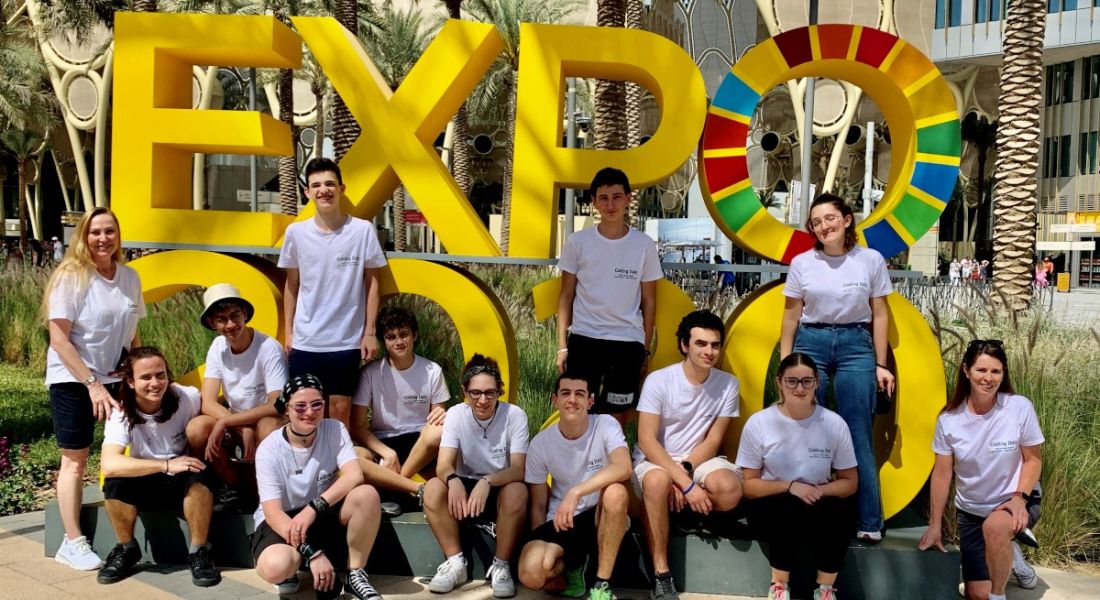 A large group of students in white T-shirts stand in front of large yellow sign that says ‘Expo’.