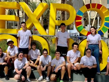 A large group of students in white T-shirts stand in front of large yellow sign that says ‘Expo’.