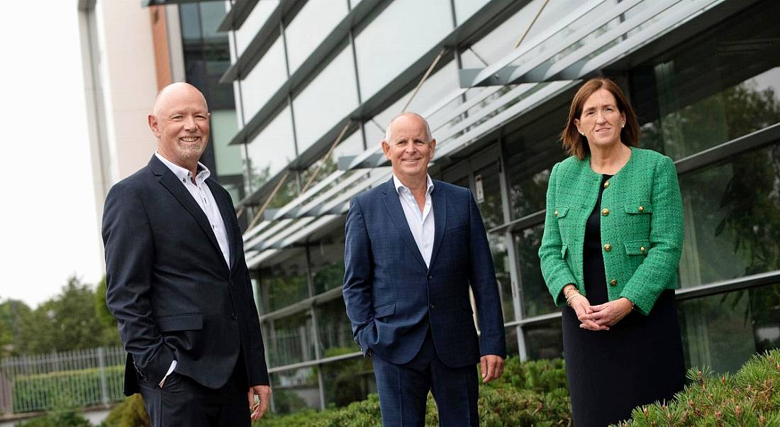 Two men and a woman standing and smiling with a building in the background. They are Dave Murphy, Brendan Jennings and Rosita Fennell of PM Group.