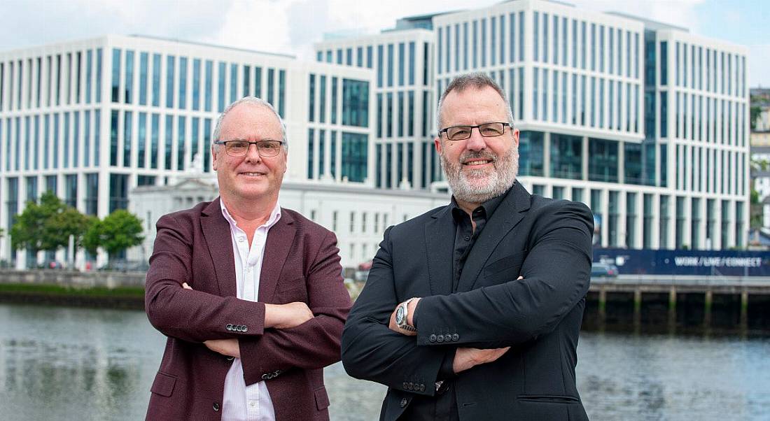 Two men who work at Douglas Control and Automation standing in front of a river with a bridge and buildings behind them.