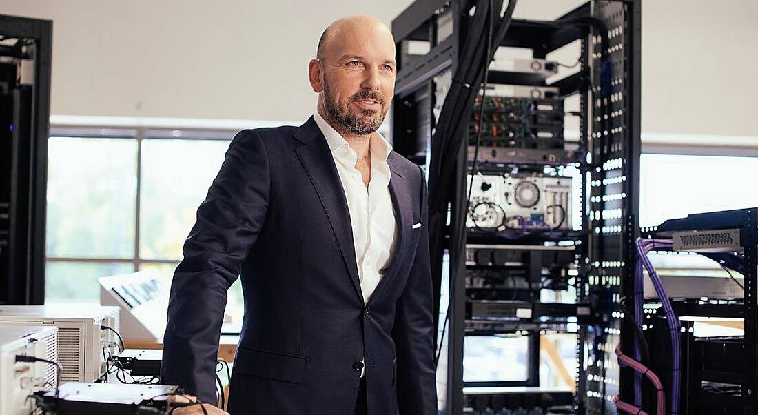 Philip Dowds of Okto Technologies stands leaning on a desk in an office with a filing cabinet behind him.