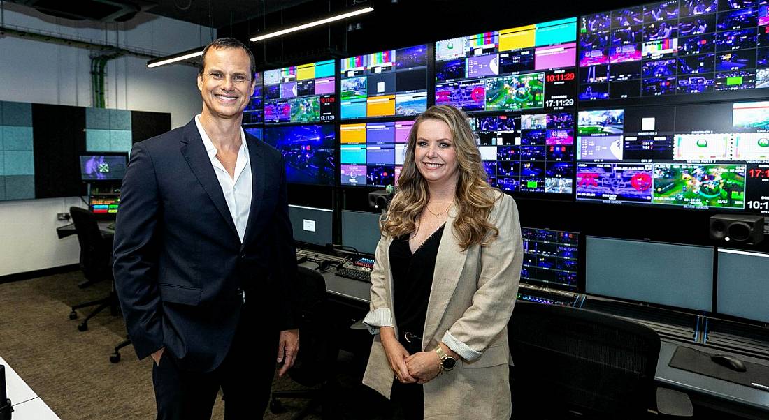 Two people stand in Riot Games' new broadcast studio in Dublin, with screens on the wall behind them.