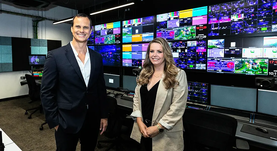 Two people stand in Riot Games' new broadcast studio in Dublin, with screens on the wall behind them.