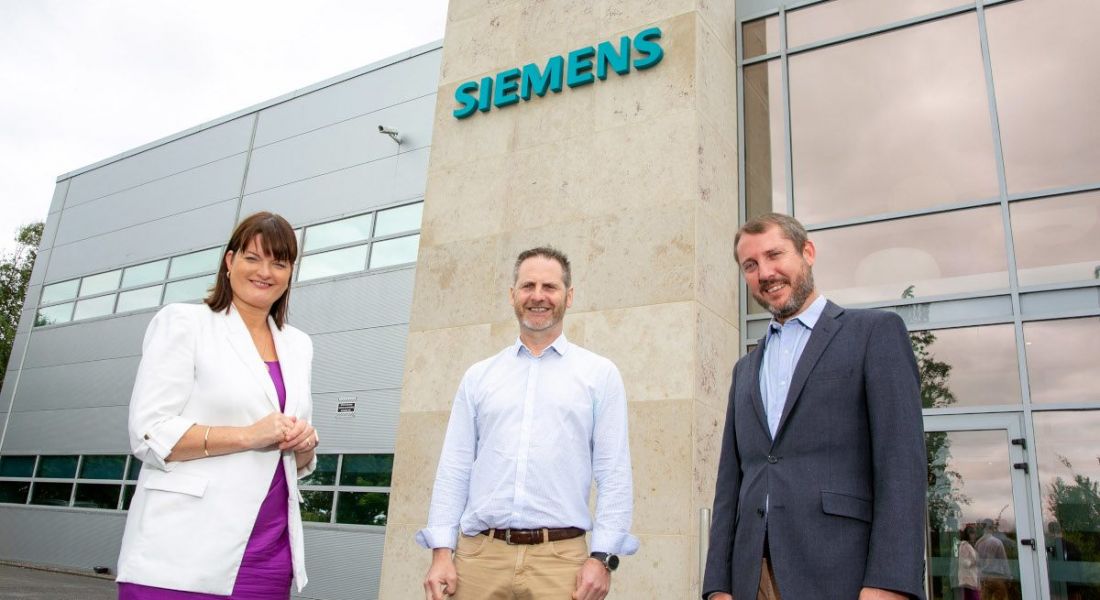 A woman and two men standing in front of a building with the Siemens logo above them.