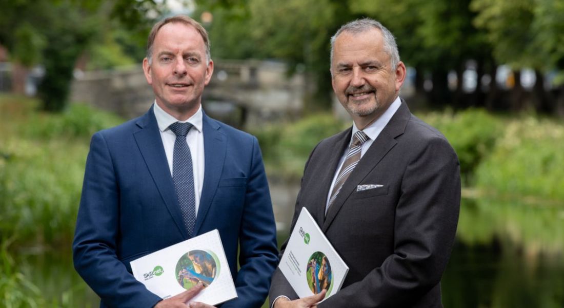 Two men holding copies of the Skillnet Ireland annual report from 2021. They are outside with trees in the background.