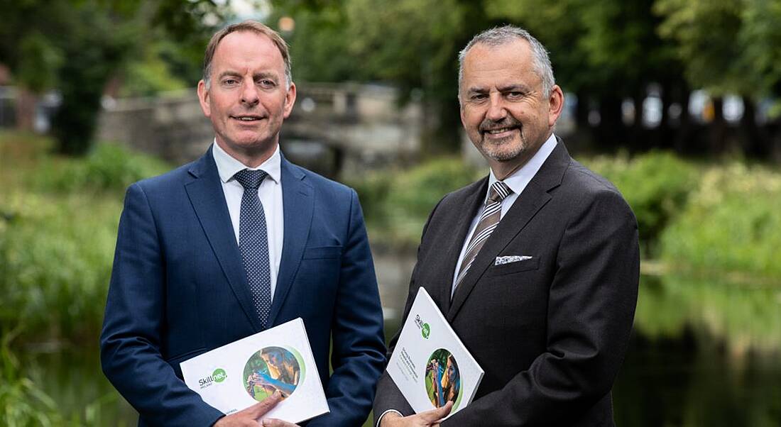 Two men holding copies of the Skillnet Ireland annual report from 2021. They are outside with trees in the background.