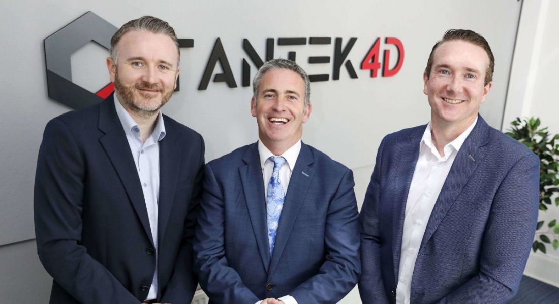 Three men in suits standing side by side in a room, with the Tantek 4D logo written on a grey wall behind them.