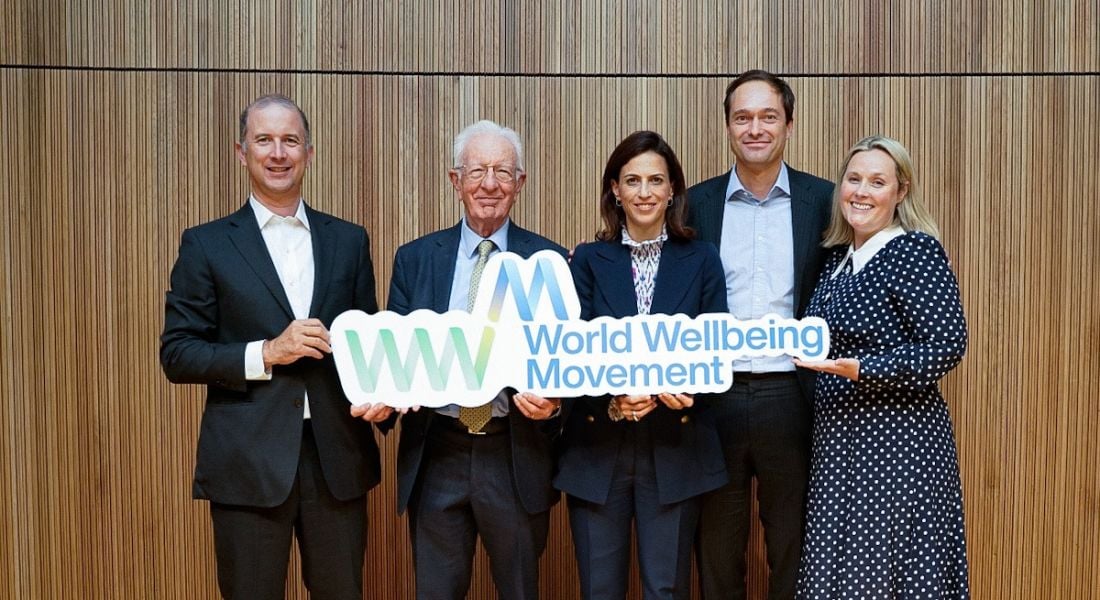 Five people stand in a line holding a sign that says World Wellbeing Movement.