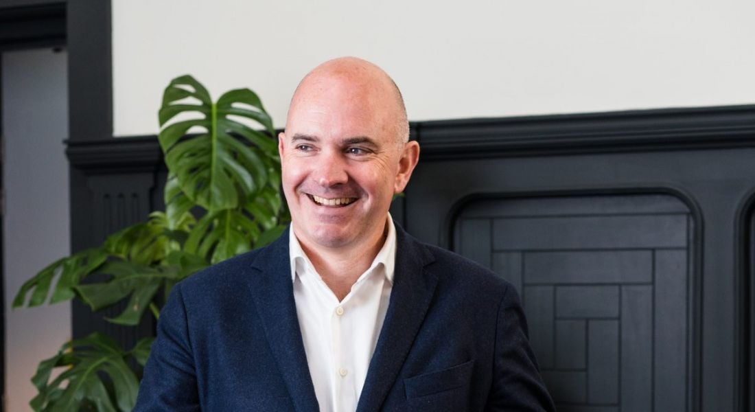 Darragh McCarthy looking away from the camera and smiling with an indoor plant in the background.