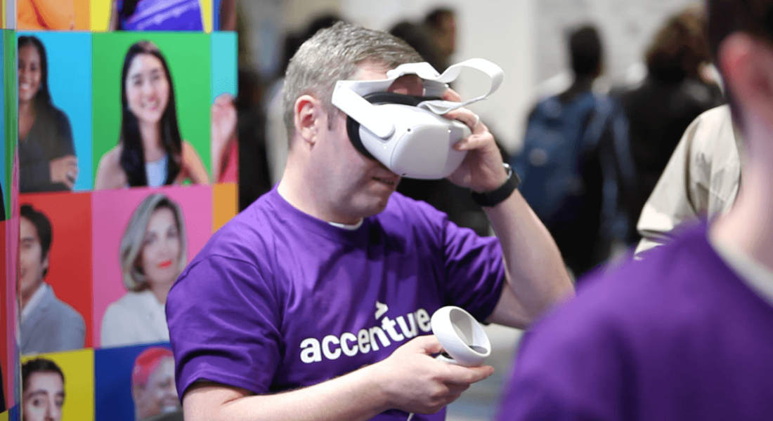A man wearing a purple Accenture t-shirt is using a VR headset, demonstrating using the metaverse.