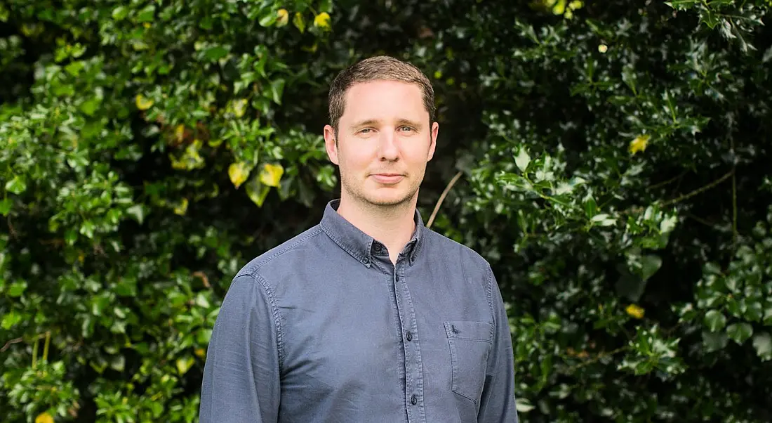 Accenture's Andrew Poole stands outside in front of a hedge.