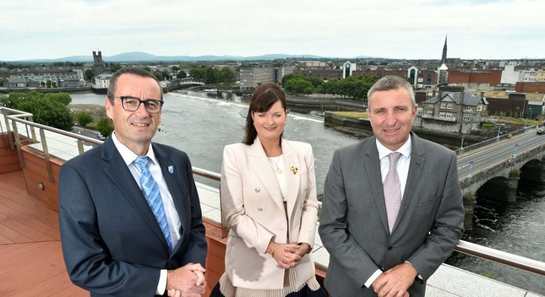 Two men and a woman in the centre standing on a balcony overlooking a city following the announcement of 50 new jobs at FileCloud.