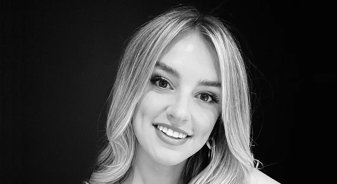 A black and white image of a young woman smiling at the camera against a dark background.