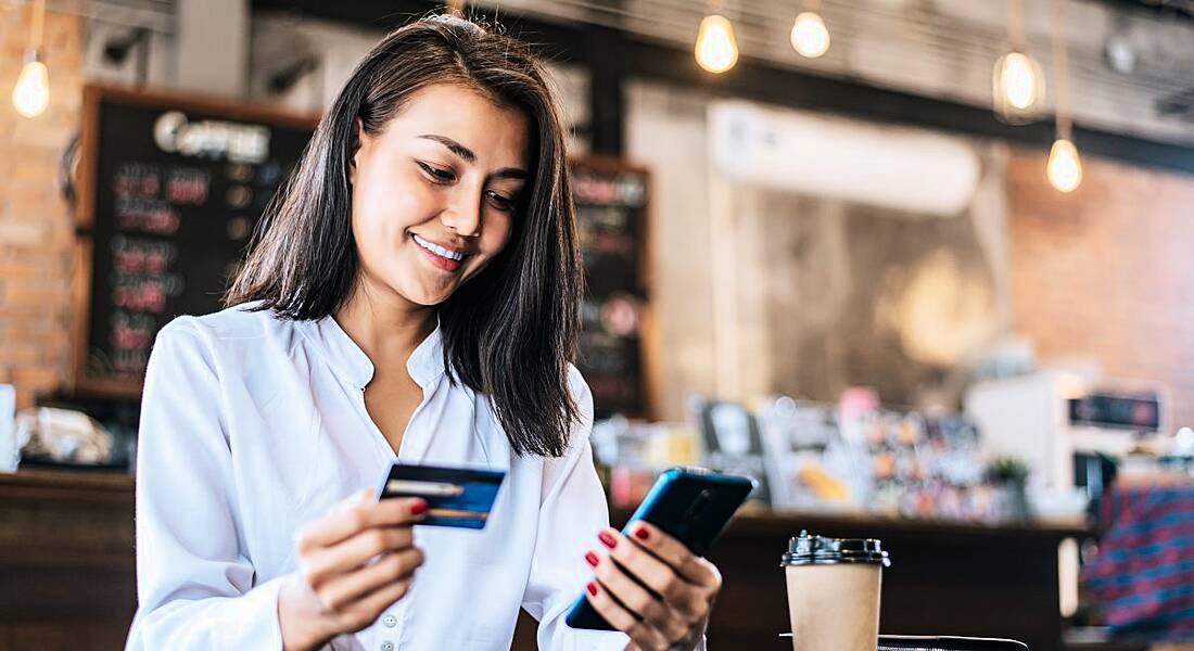 Woman using a credit card and smartphone in a cafe to pay digitally.