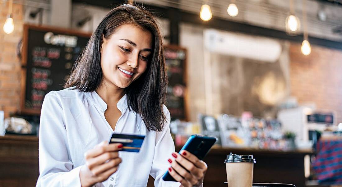 Woman using a credit card and smartphone in a cafe to pay digitally.